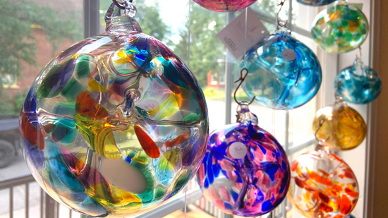 Colourful hand blown glass witch balls hang at different heights in the window of Gray Art Glass gallery.